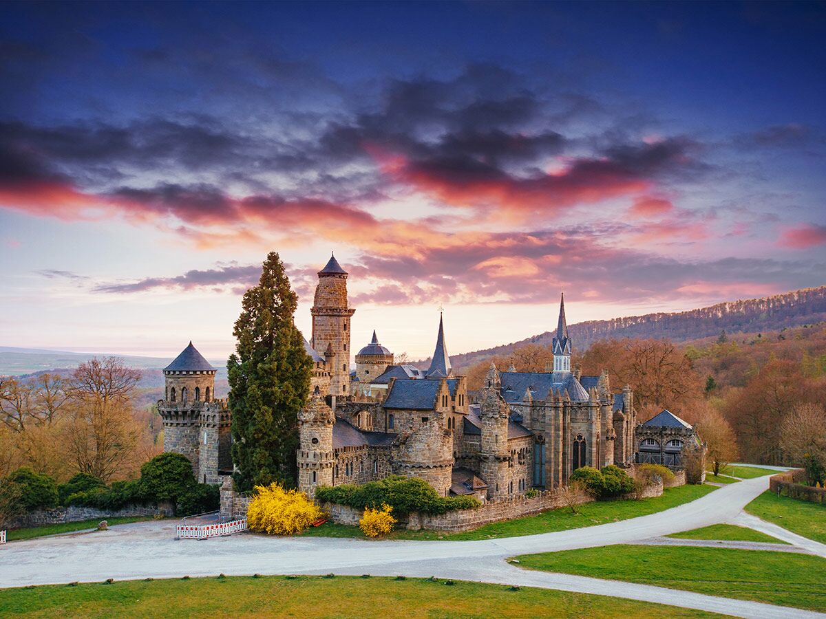 Die Löwenburg im Bergpark Wilhelmshöhe bei Sonnenuntergang, umgeben von Bäumen und dramatischem Himmel.