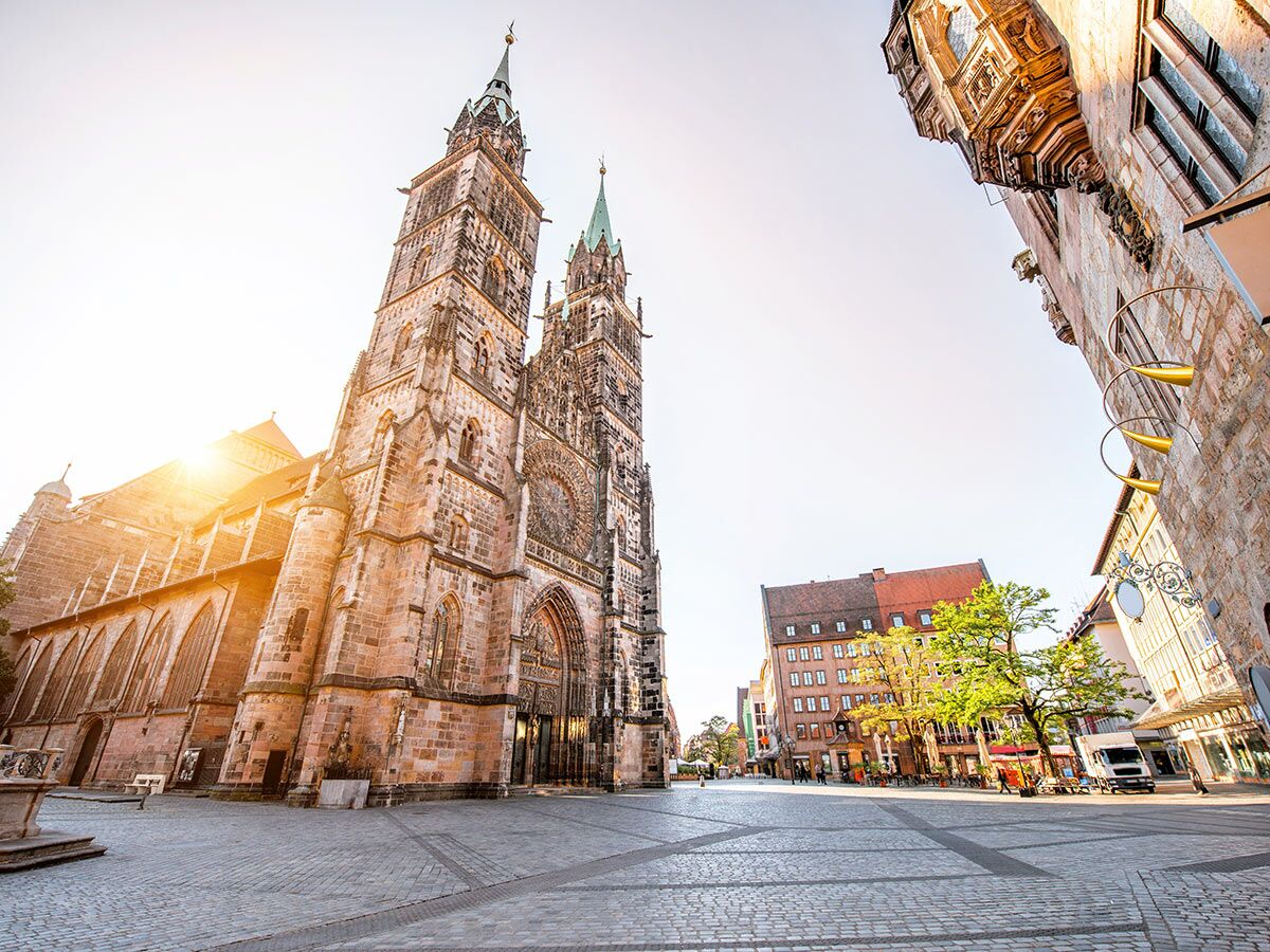 Historische Sebalduskirche in Nürnberg bei Sonnenlicht. Pflasterplatz, alte Gebäude und Bäume im Stadtzentrum.