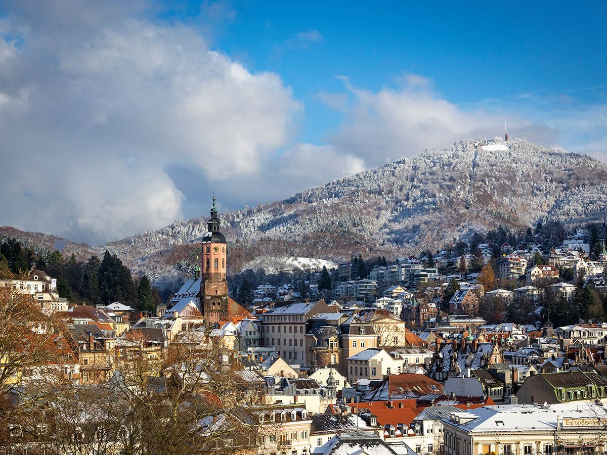Panoramablick auf die verschneite Stadt Baden-Baden mit Stiftskirche und Merkurberg unter blauem Winterhimmel.