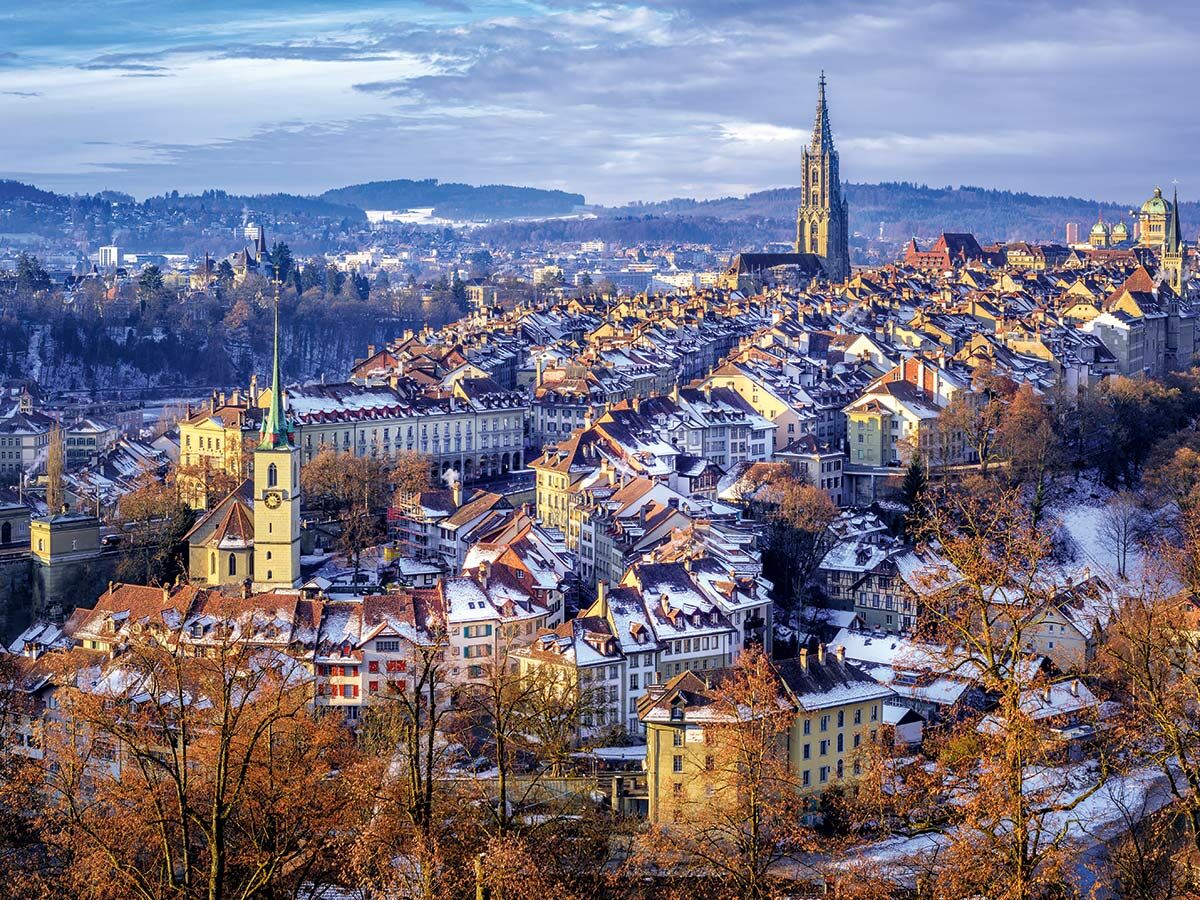 Verschneite Berner Altstadt im Winter mit historischer Architektur, Berner Münster, Nydeggkirche und der Aare in der Abendsonne.