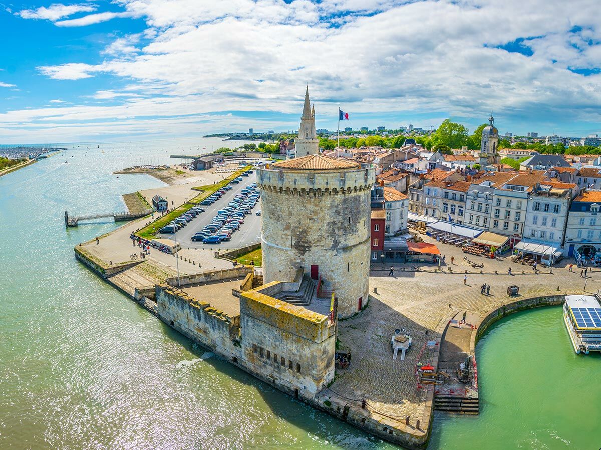 Luftaufnahme von La Rochelle mit Saint-Nicolas Turm, historischem Hafen, Stadtgebäuden und Meer unter blauem Himmel.