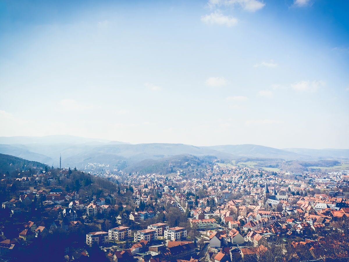 Panoramablick auf eine historische deutsche Stadt mit roten Dächern in einem Tal, umgeben von bewaldeten Hügeln unter blauem Himmel.