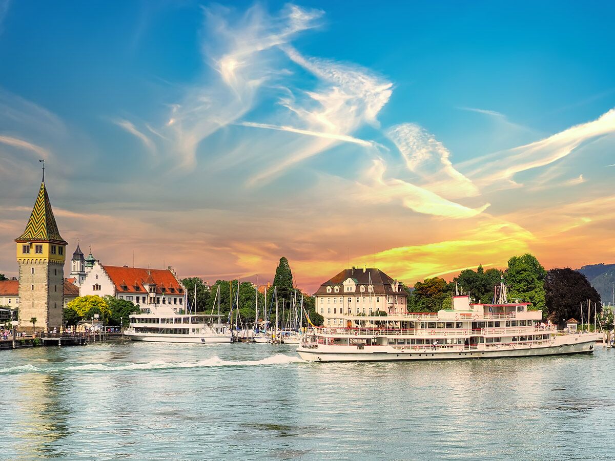 Blick auf den Lindauer Hafen am Bodensee bei Sonnenuntergang mit Leuchtturm, Passagierschiff und Yachten.
