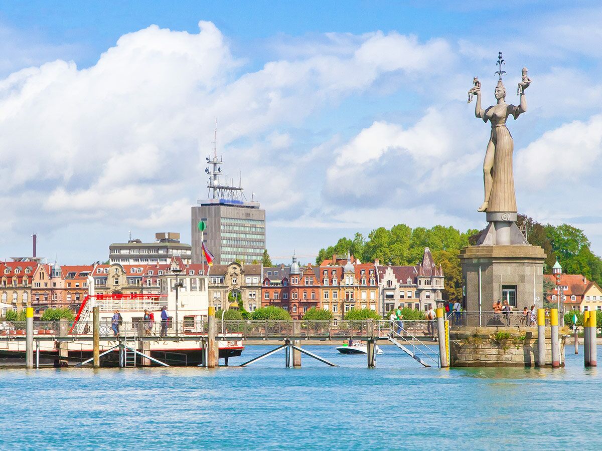 Statue Imperia im Hafen von Konstanz am Bodensee, umgeben von historischen Gebäuden, Booten und blauem Himmel.