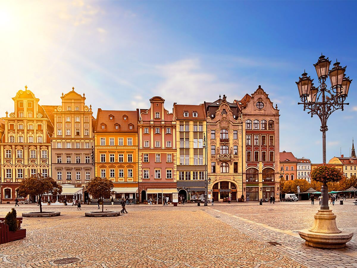 Blick auf den historischen Marktplatz von Wrocław mit farbenfrohen Giebelhäusern, Kopfsteinpflaster und Menschen unter blauem Himmel.