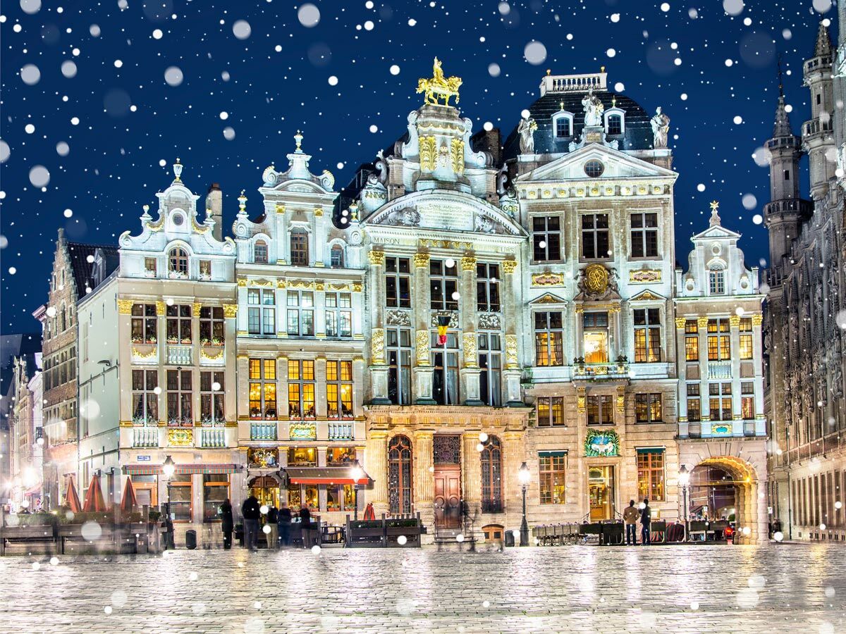 Historische Gildehäuser am Grand Place Brüssel bei Nacht im Schneefall, beleuchtet mit warmem Licht und goldenen Verzierungen.