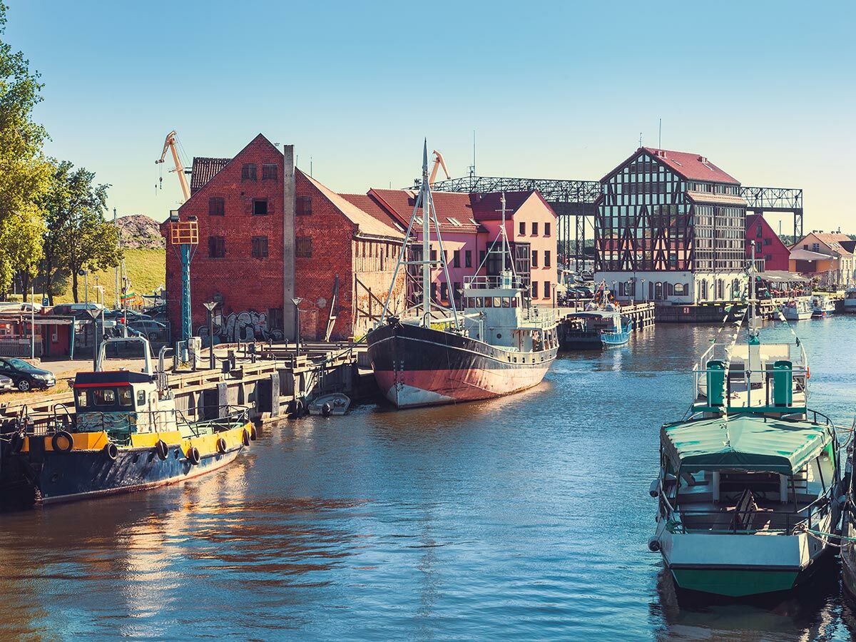 Belebtes Hafenviertel mit Booten, historischen Backsteingebäuden und modernen Bauten am Kanal unter blauem Himmel.