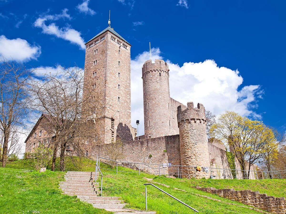 Historische Burg Breuberg mit hohen Steintürmen auf einem grünen Hügel unter blauem Himmel mit Wolken.