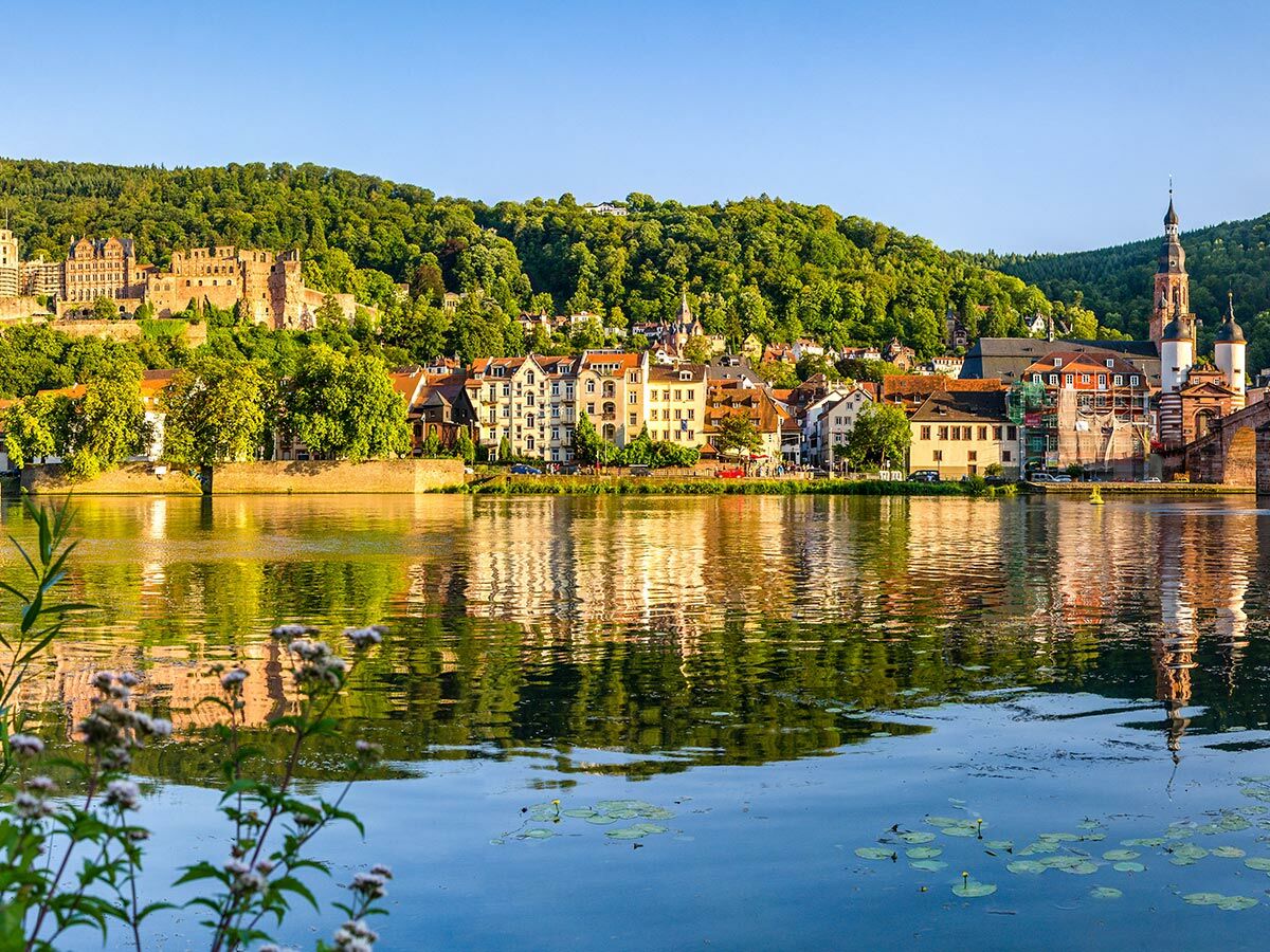 Panoramablick auf das Heidelberger Schloss, die Altstadt und den Neckar mit Brücke bei Sonnenlicht und Reflexionen.