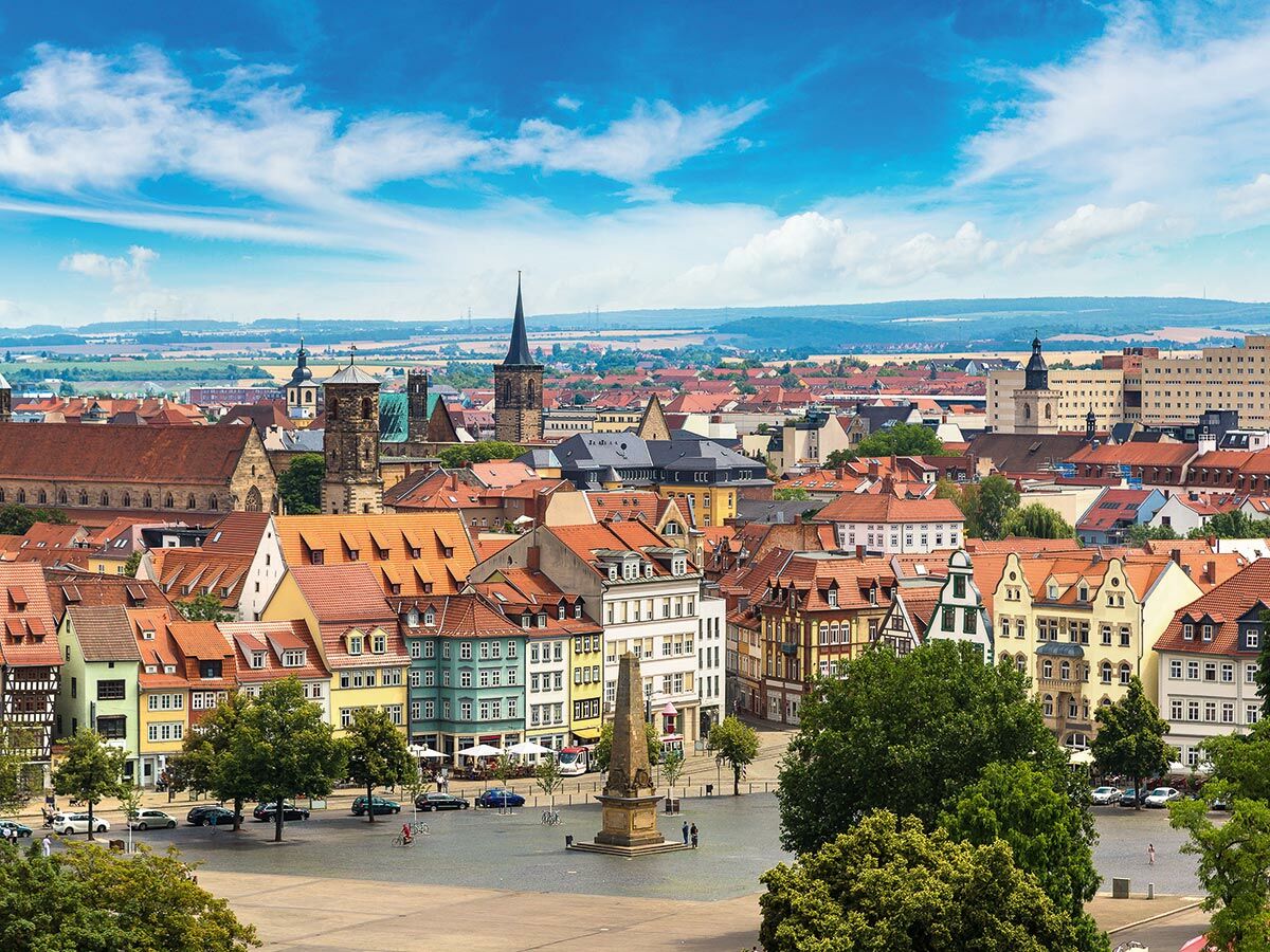 Luftaufnahme der historischen Altstadt von Erfurt mit Domplatz, bunten Häusern und Kirchen unter blauem Himmel.