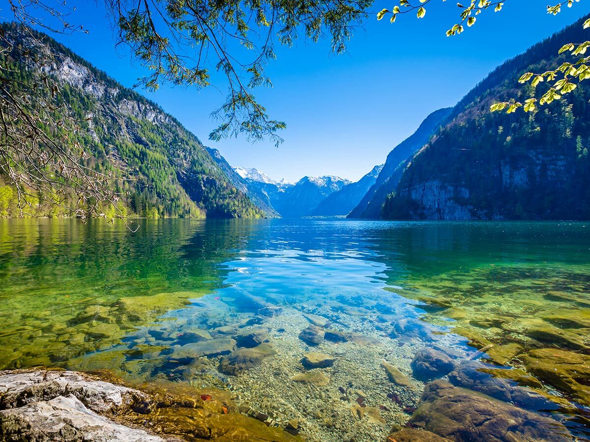 Idyllischer Bergsee Königssee mit kristallklarem Wasser, umgeben von grünen Wäldern und schneebedeckten Alpen Gipfeln.