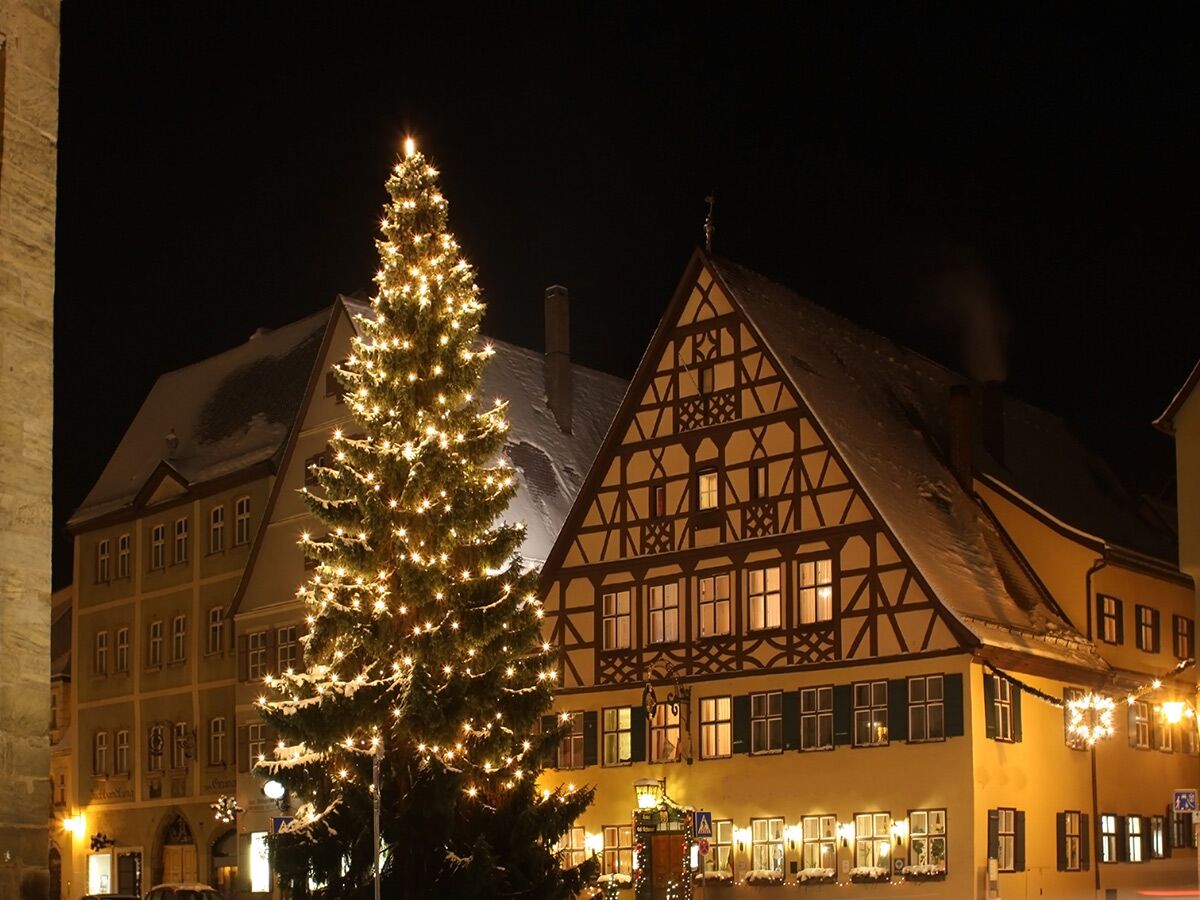 Beleuchteter Weihnachtsbaum auf verschneitem Marktplatz einer historischen Altstadt in Deutschland bei Nacht. Weihnachtsstimmung mit Lichterglanz.