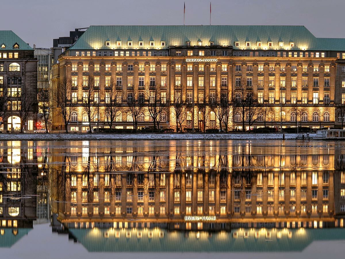 Das historische Hapag-Lloyd Gebäude in Hamburg bei Nacht, dessen beleuchtete Fenster sich im stillen Wasser spiegeln.