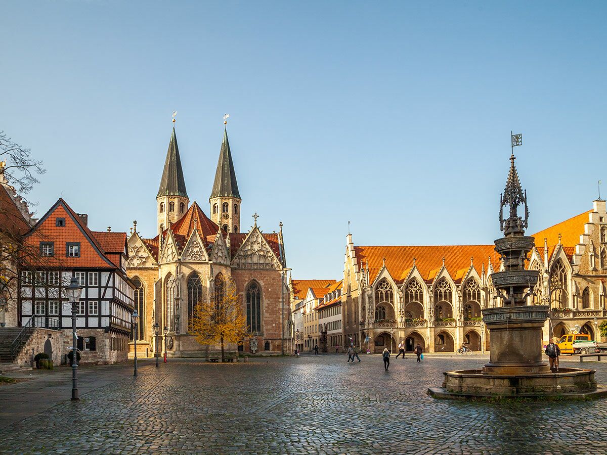 Braunschweiger Burgplatz mit St. Blasii-Dom, Altstadtrathaus, Fachwerkhaus und Heinrichsbrunnen bei blauem Himmel.
