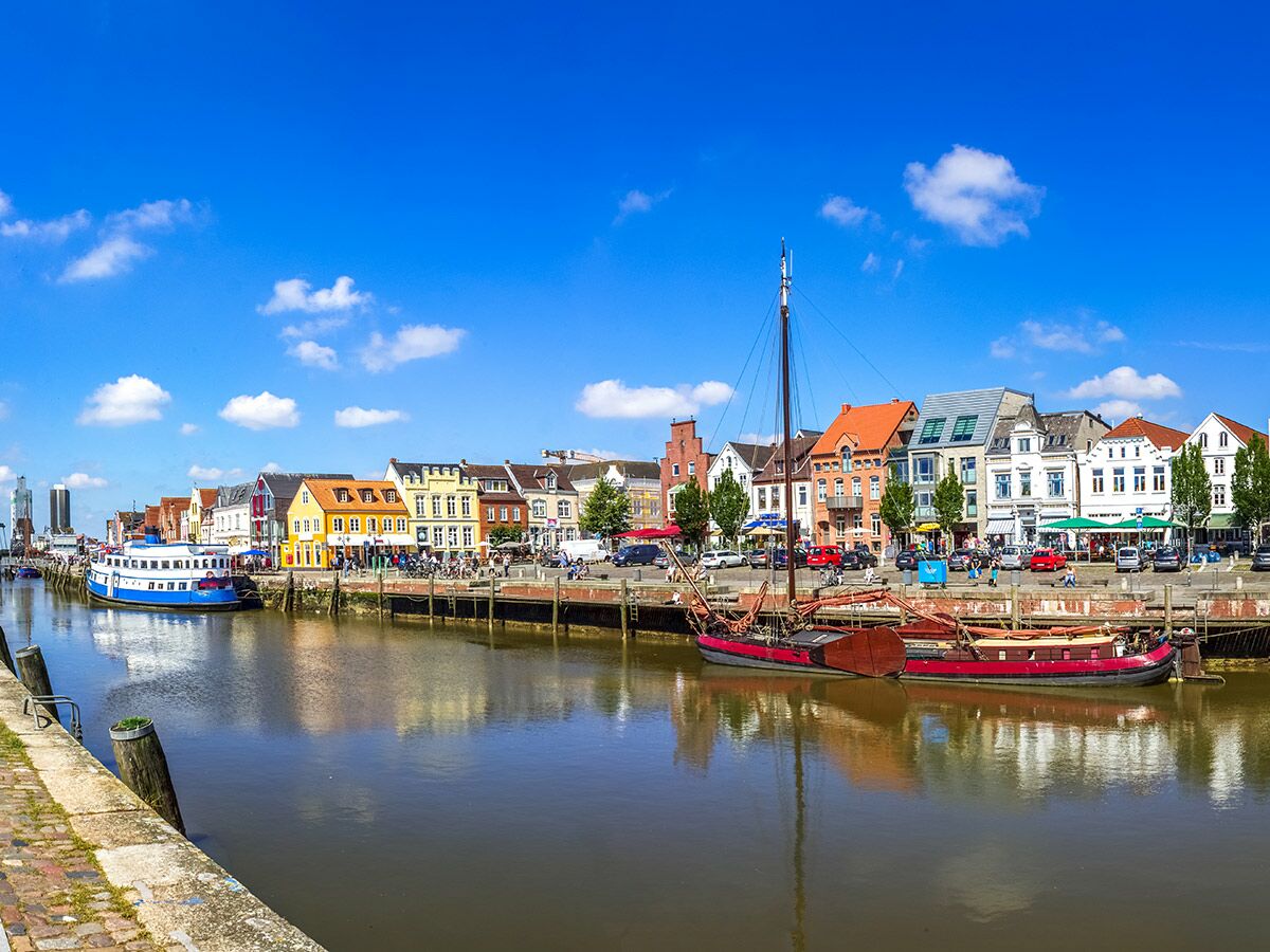 Panoramablick auf die Gracht in Friedrichstadt mit farbenfrohen Giebelhäusern, historischen Booten und blauem Himmel.