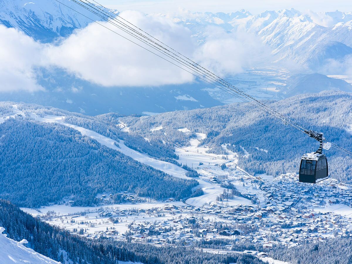 Panoramablick auf verschneite Alpen, ein Winterdorf und eine Gondelbahn über einem Skigebiet.