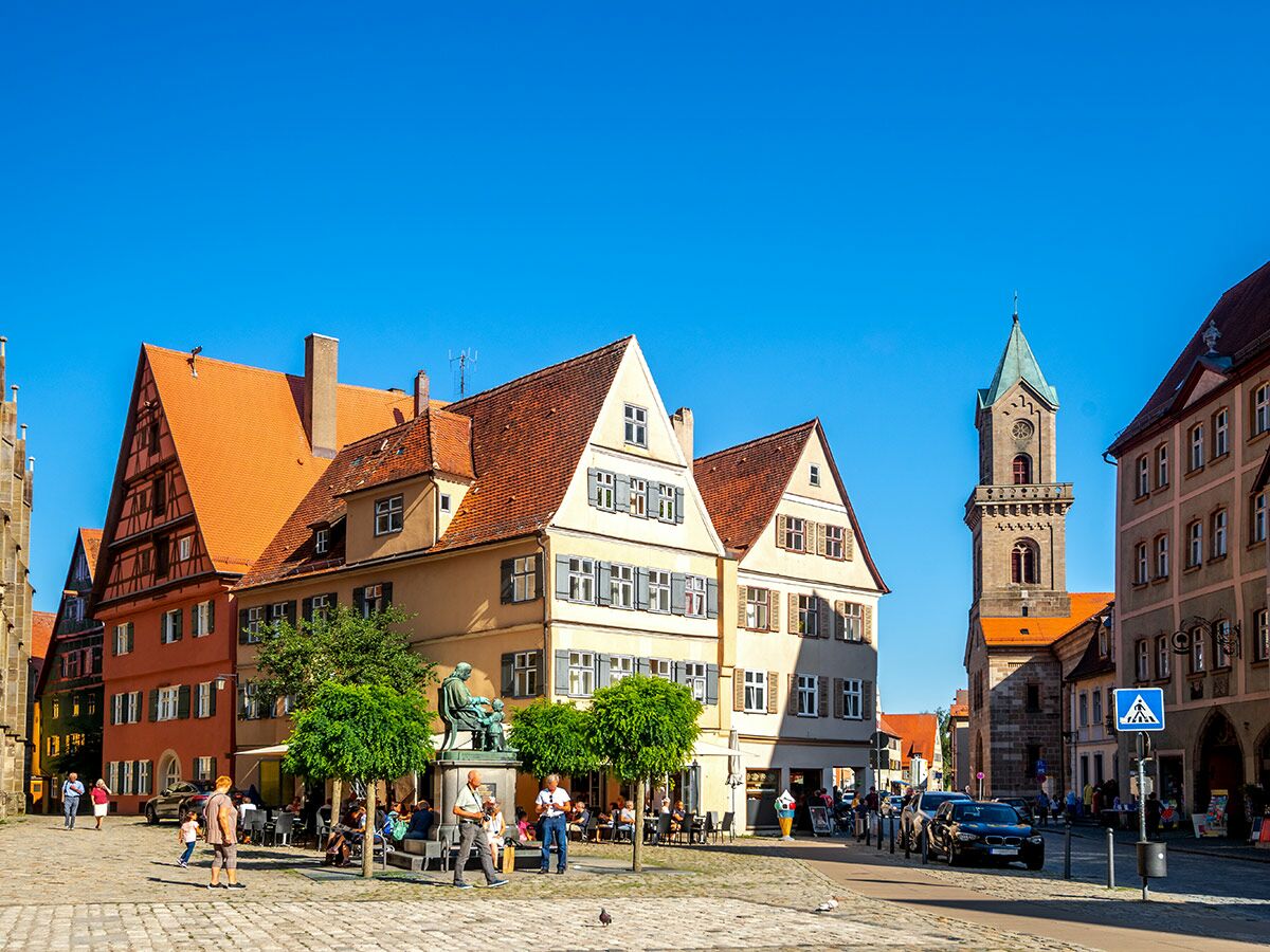 Blick auf den historischen Marktplatz von Schwäbisch Hall mit Fachwerkhäusern, Kirchturm, Eduard-Mörike-Statue und belebten Cafés bei Sonnenschein.