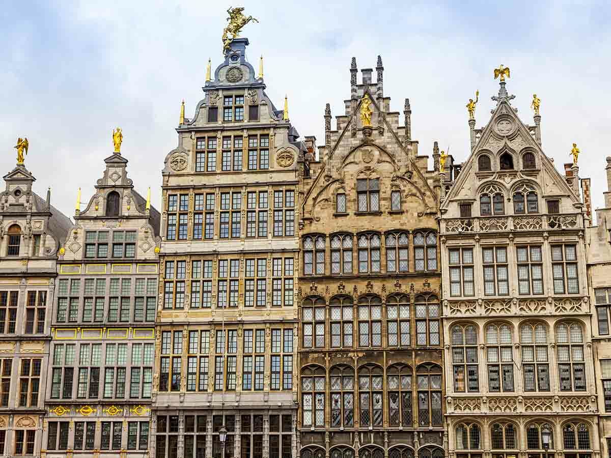 Reihe historischer, verzierter Giebelhäuser in Antwerpen mit goldenen Statuen auf den Dächern und vielen Fenstern.