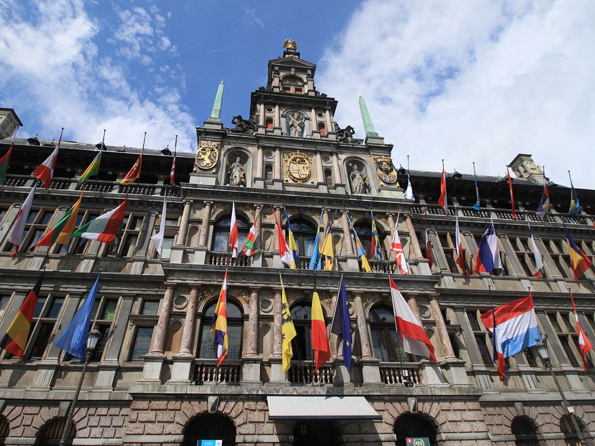 Historisches Rathaus in Antwerpen, Belgien, geschmückt mit zahlreichen internationalen und europäischen Flaggen unter blauem Himmel.