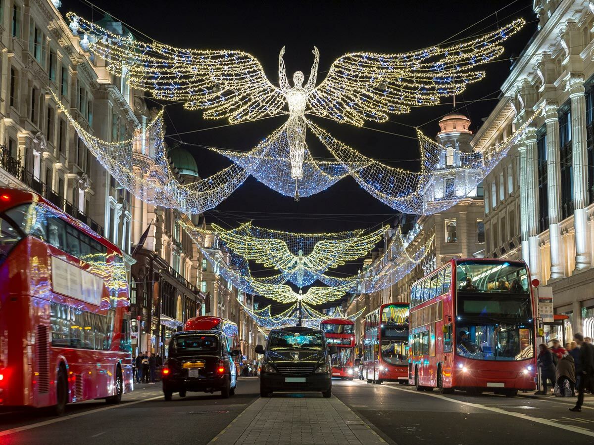 Weihnachtliche Regent Street in London bei Nacht mit Engeln aus Lichtern, roten Doppeldeckerbussen und Passanten.