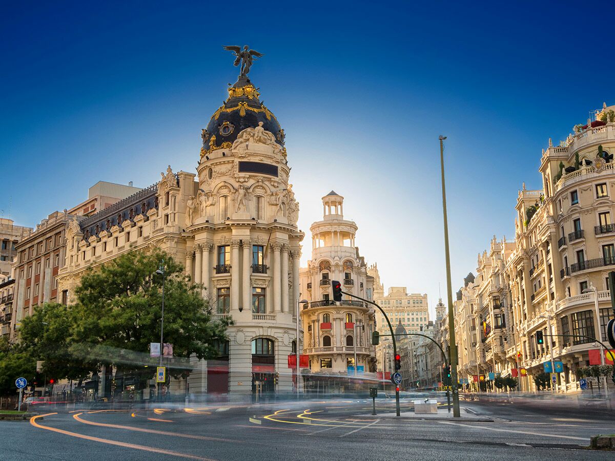 Majestätisches Metropolis Gebäude und belebte Gran Vía in Madrid bei Sonnenaufgang mit Lichtspuren des Verkehrs.