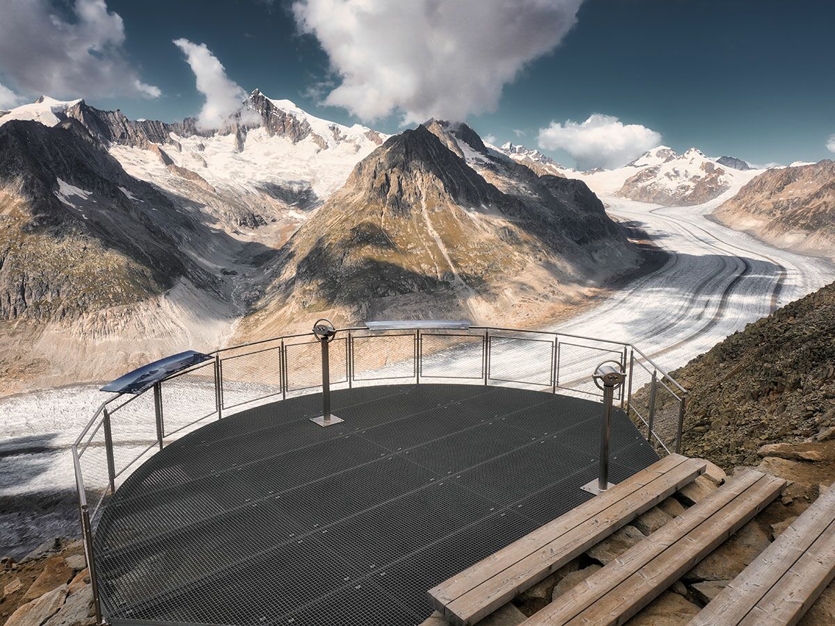 Panoramablick auf den Aletschgletscher von einer modernen Aussichtsplattform mit Ferngläsern und Bergen.
