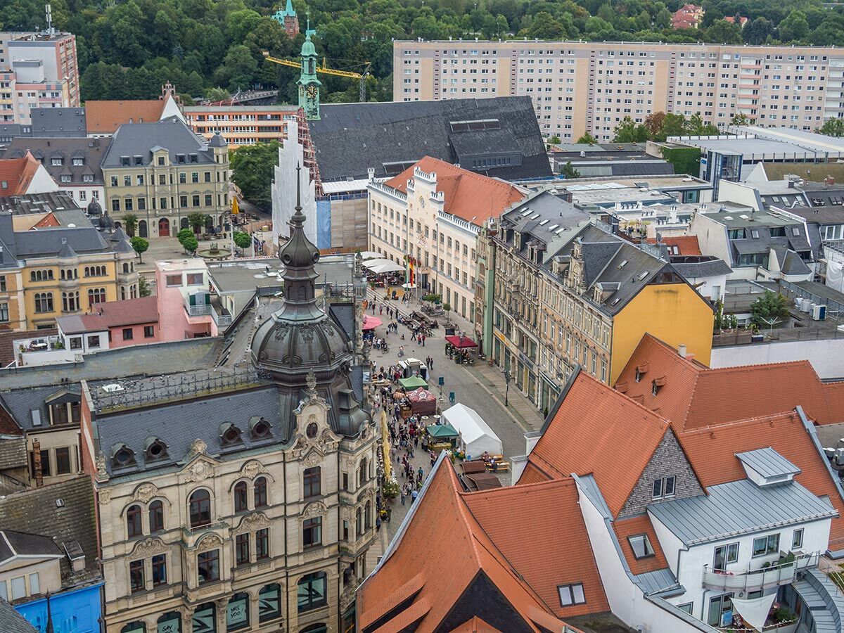 Luftbild von Chemnitz mit belebtem Marktplatz, historischen Gebäuden, modernen Wohnblöcken und grünen Wäldern.