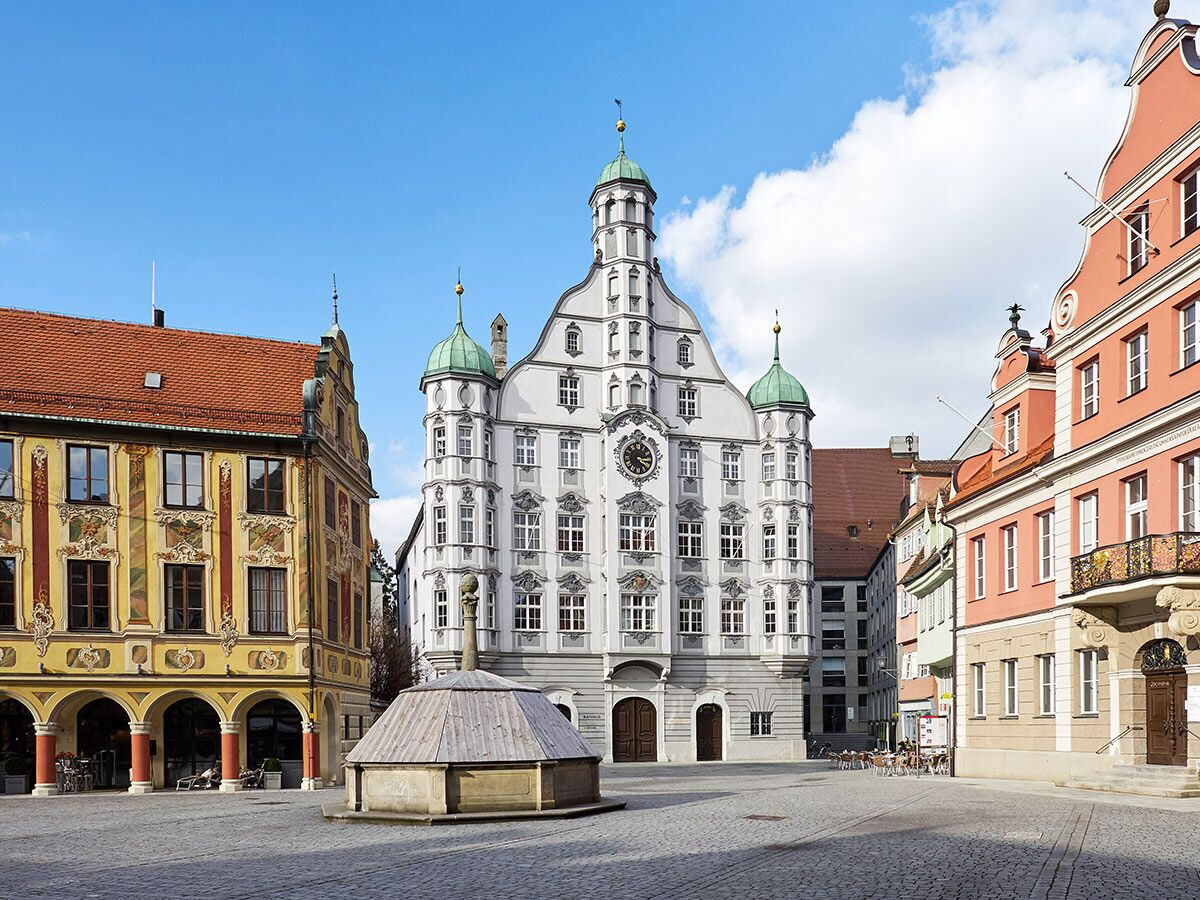 Historisches Rathaus Memmingen am sonnigen Stadtplatz. Renaissance-Architektur, Brunnen, farbige Bürgerhäuser, blauer Himmel.