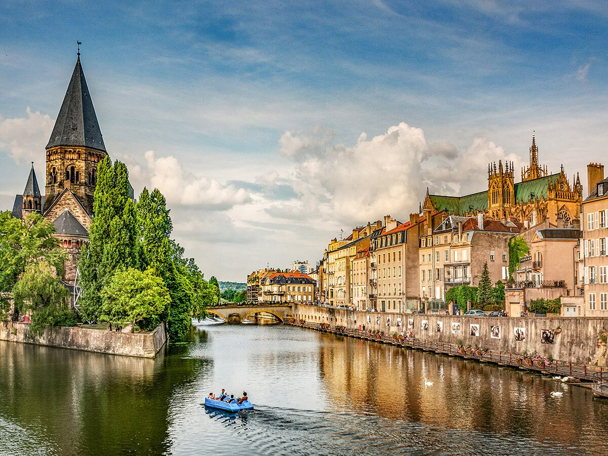 Historische Stadtansicht von Metz, Frankreich, mit dem Temple Neuf, der Kathedrale, dem Fluss Mosel, einem Boot und Uferpromenade.