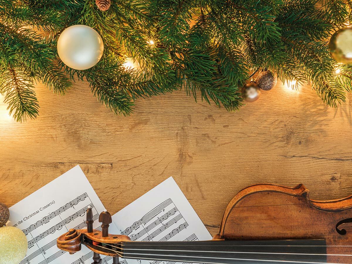 Festlicher Weihnachtshintergrund mit Tannenbaumzweigen, Lichterkette, Kugeln und Notenblatt für Violine auf Holz.