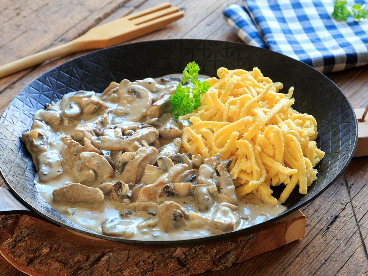 Jägerschnitzel mit cremiger Pilzrahmsoße und Spätzle in einer schwarzen Pfanne auf rustikalem Holztisch.