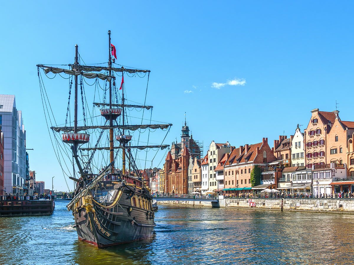 Großes Piratenschiff auf der Motława in Danzig, umgeben von historischen Giebelhäusern und belebter Promenade bei Sonnenschein.