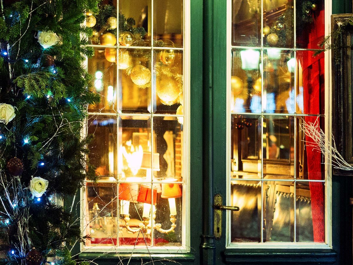 Detail eines weihnachtlich dekorierten Schaufensters mit leuchtendem Christbaum, goldenen Kugeln und warmen Lichtern im Inneren.