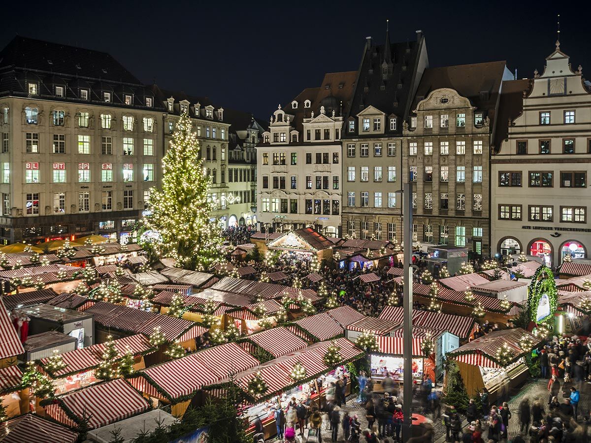 Luftaufnahme des Leipziger Weihnachtsmarkts bei Nacht mit festlich beleuchteten Ständen, großem Christbaum und vielen Besuchern.