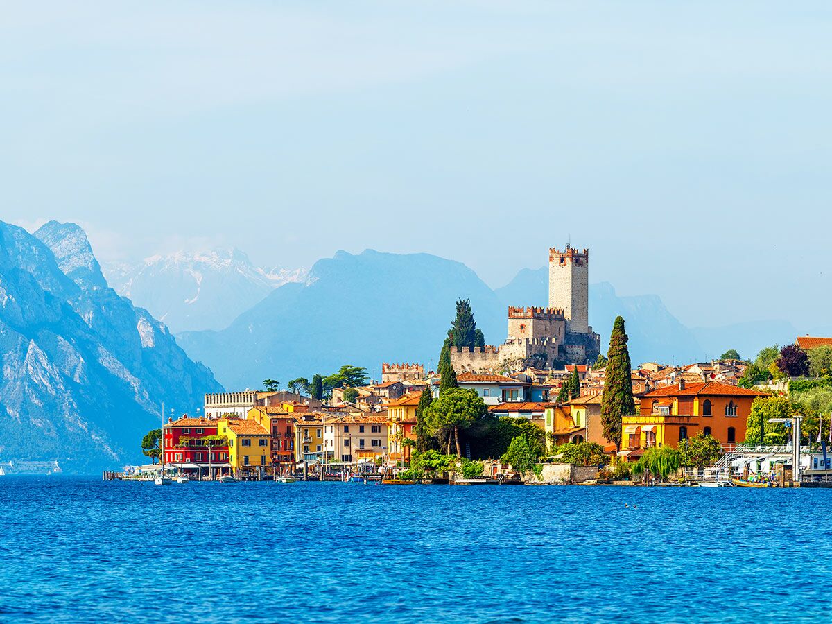 Malerische Stadt Malcesine am Gardasee mit farbenfrohen Häusern, Scaliger Schloss und schneebedeckten Alpen im Hintergrund.