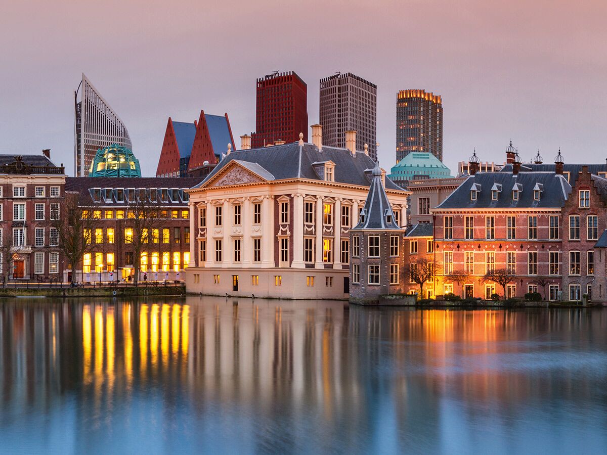 Abendansicht des Hofvijver in Den Haag mit historischen Gebäuden wie dem Mauritshuis und modernen Hochhäusern, deren Lichter sich im Wasser spiegeln.
