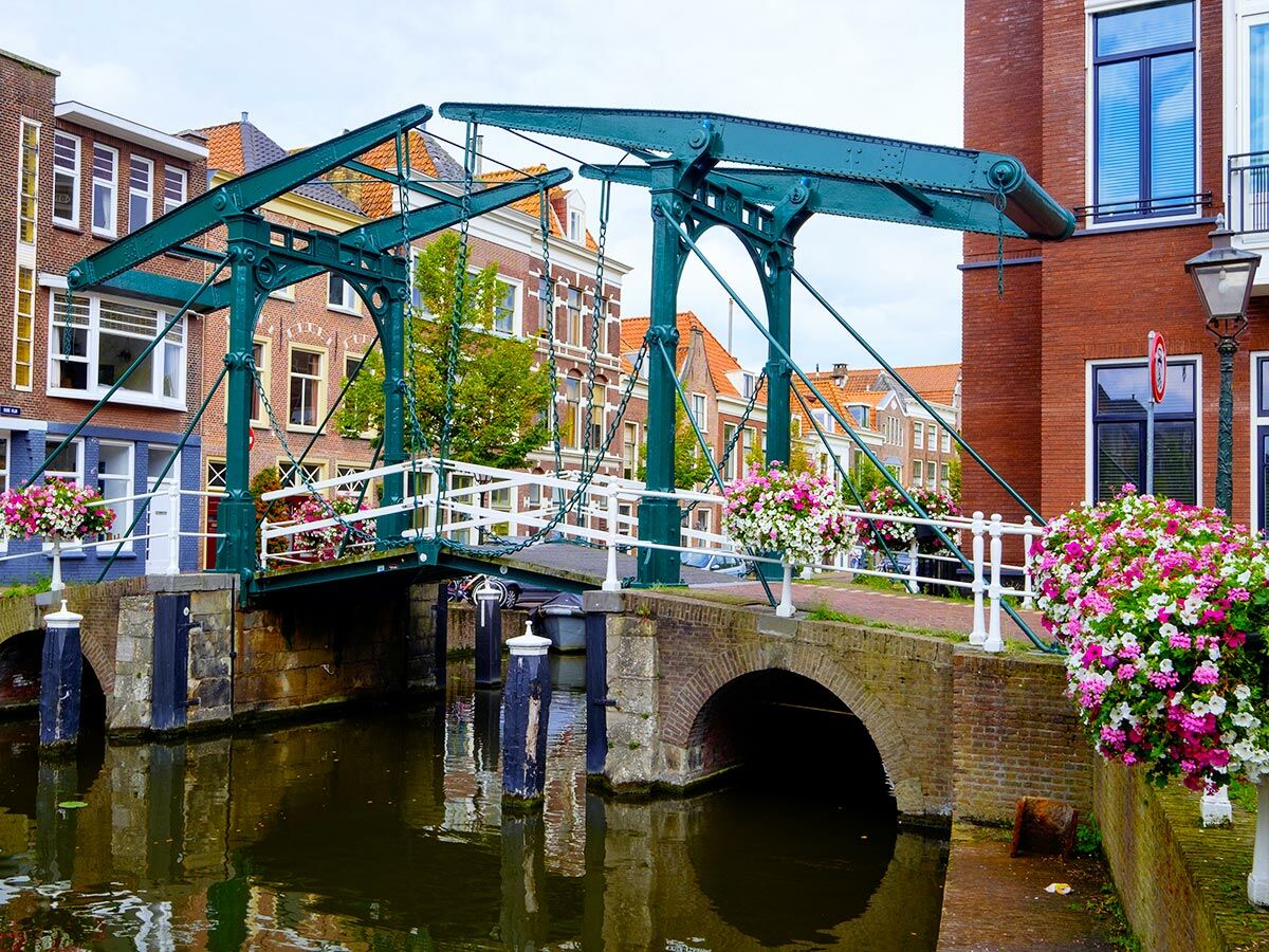 Historische grüne Zugbrücke über einem Kanal mit bunten Blumenkästen und traditionellen Ziegelhäusern in einer niederländischen Stadt.