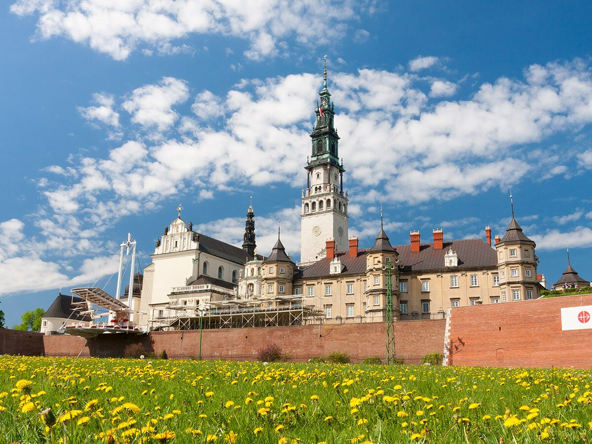 Jasna Góra Kloster Częstochowa, Polen, mit hohem Turm, historischen Gebäuden, Dächern, grüner Wiese und Löwenzahn.