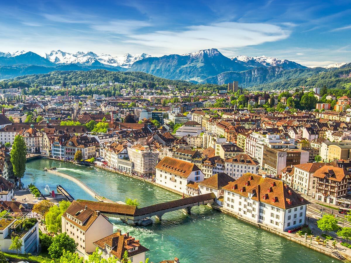 Panoramablick auf die Stadt Luzern mit Reuss, Kapellbrücke, historischen Gebäuden und verschneiten Alpen im Hintergrund.