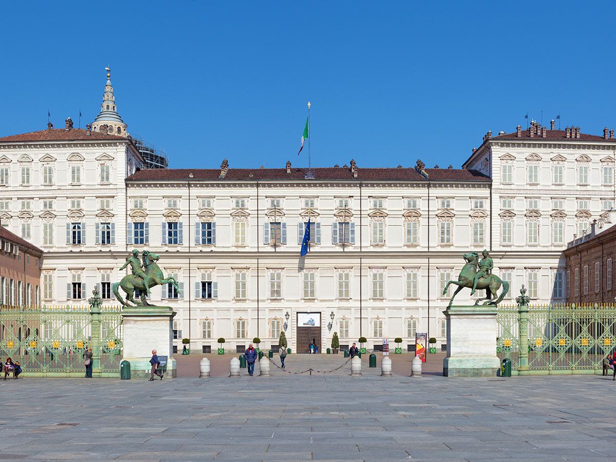 Blick auf den Königspalast von Turin (Palazzo Reale) an einem sonnigen Tag mit zwei Reiterstatuen und Menschen auf der Piazza Castello.
