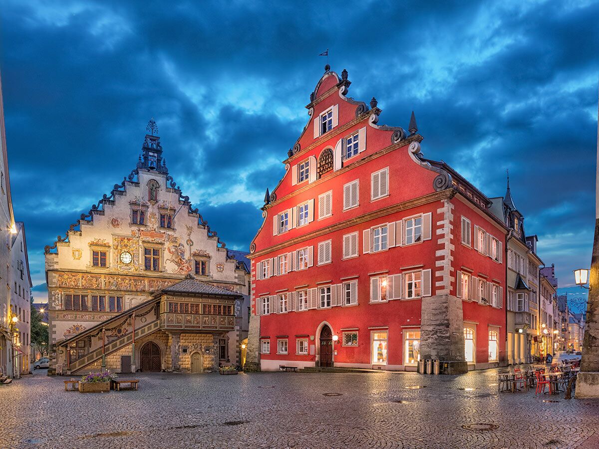 Historisches Altes Rathaus und Humpis-Haus in Ravensburg bei Abenddämmerung, beleuchteter Marienplatz mit Kopfsteinpflaster.
