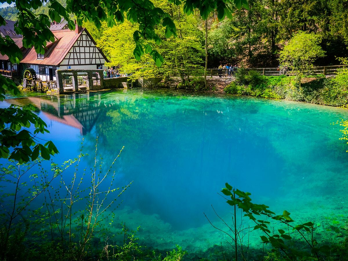 Atemberaubender Blautopf in Blaubeuren, Deutschland, mit historischer Mühle und türkisblauem Wasser, umgeben von grüner Natur.
