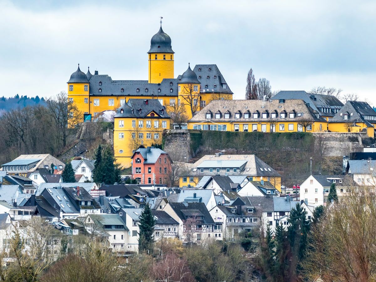 Schloss Waldeck in Hessen, Deutschland, thront als gelbes historisches Gebäude über einer Stadt im Winter.