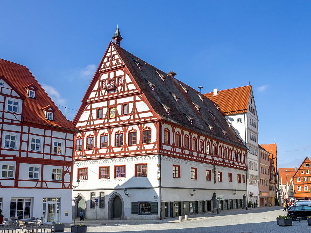 Prominentes rot-weißes Fachwerkhaus mit Spitzdach und Storchennest, umgeben von historischen Gebäuden an sonnigem Marktplatz.