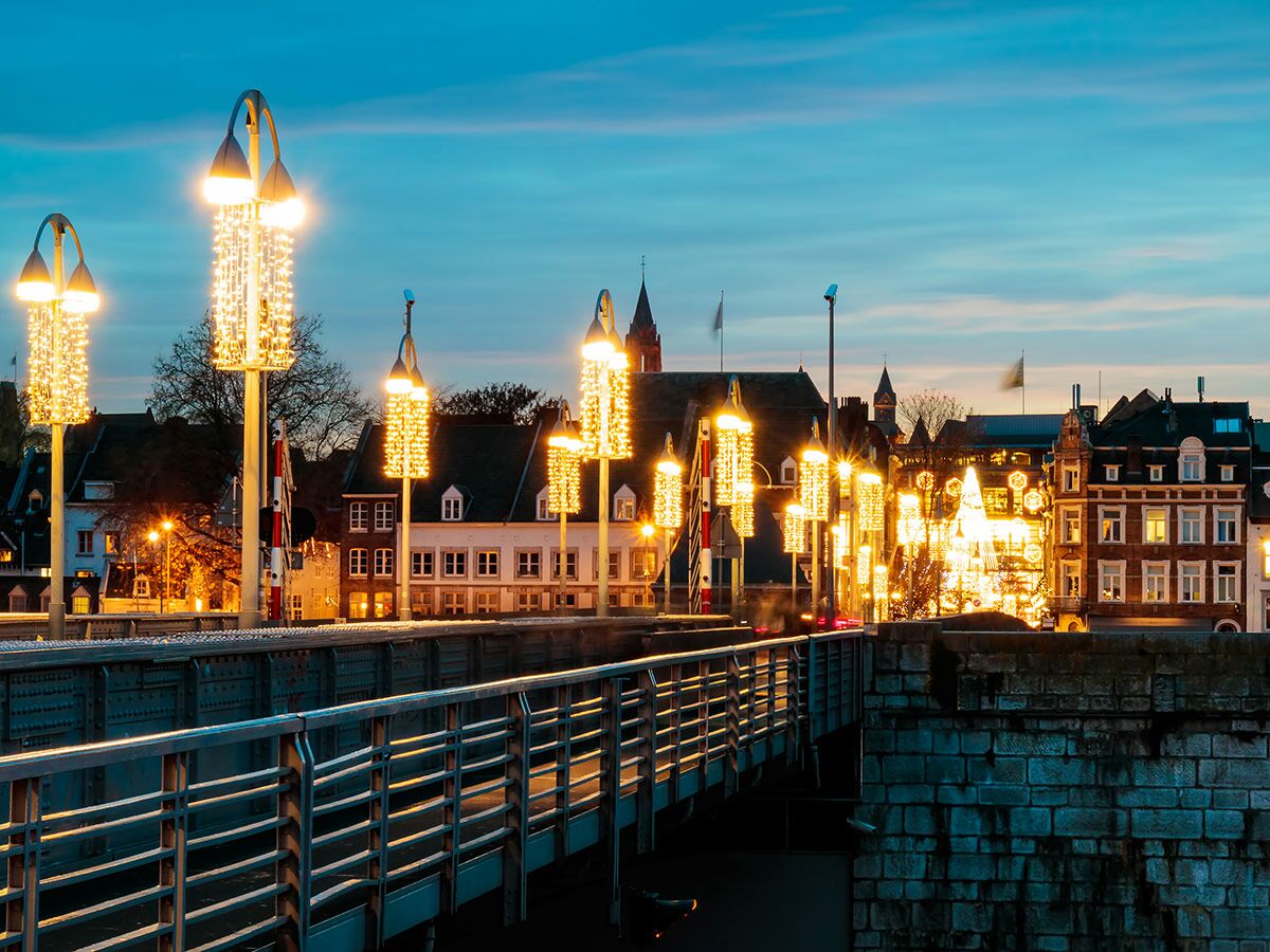 Festlich beleuchtete Brücke mit funkelnden Lichterketten und Altstadt bei Abenddämmerung.