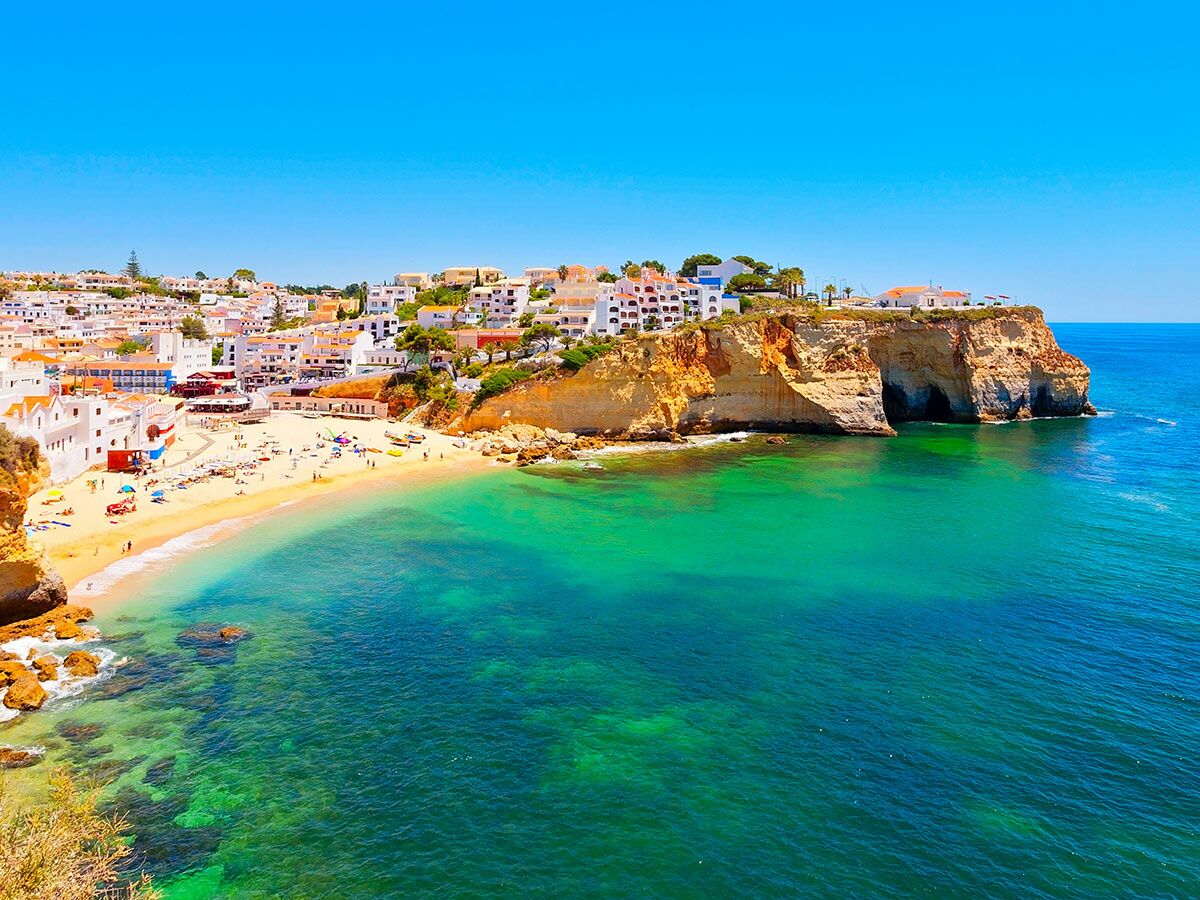 Panoramablick auf den malerischen Strand Praia do Carvoeiro in Portugal mit weißen Häusern auf Klippen und türkisblauem Meer.