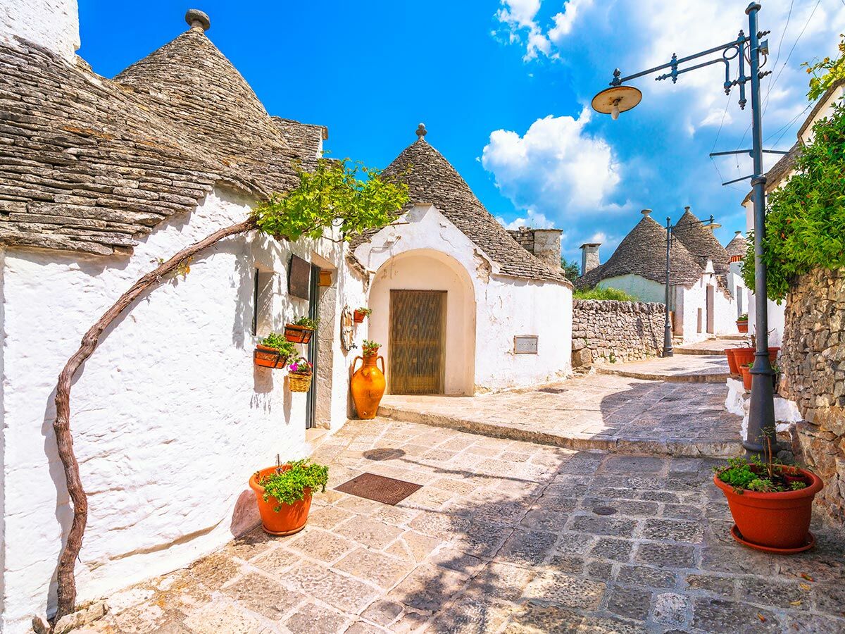 Sonniger Blick auf eine malerische Gasse zwischen traditionellen, weiß getünchten Trulli Häusern mit kegelförmigen Dächern in Alberobello, Italien.