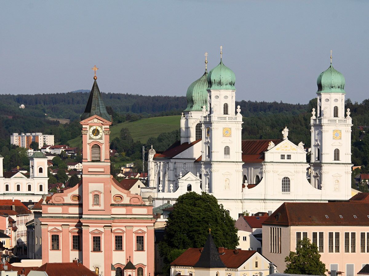 Panoramablick auf Passau mit dem Dom St. Stephan und der St. Michael Kirche vor grünen Hügeln und blauem Himmel.