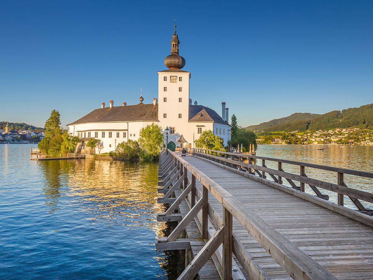 Schloss Ort in Gmunden am Traunsee, Österreich, mit einer langen Holzbrücke über das Wasser bei Abendlicht.