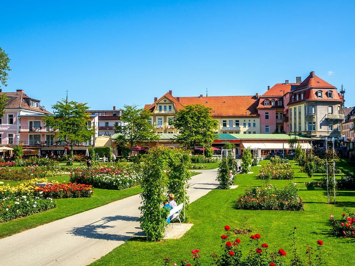 Blühender Rosengarten mit farbigen Rosen, grünen Wiesen und historischen Gebäuden an einem sonnigen Tag in einer deutschen Stadt.